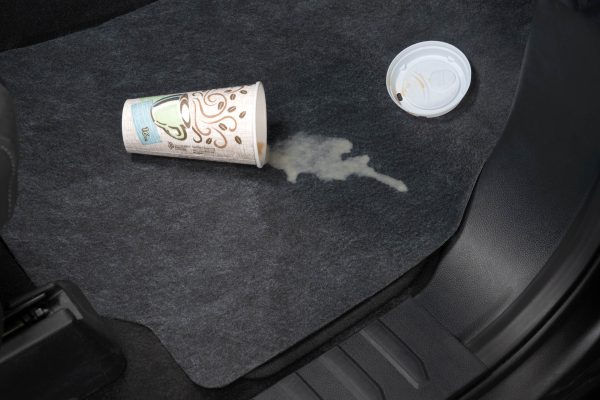 A disposable coffee cup tipped and spilt on the floor mat showing absorption and protecting the car floor.