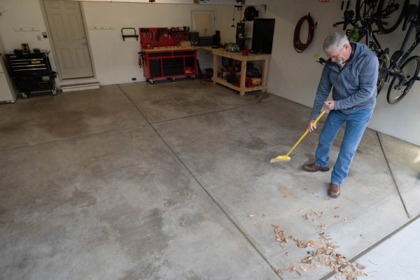 A man preparing the garage floor by sweeping and cleaning it to apply the multi-surface protector.