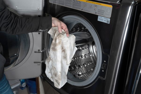 A person holding a dirty Ragboss washable rag near an open washing machine.