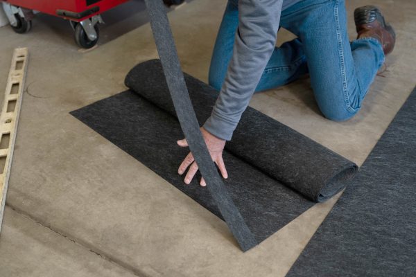 A person cutting the Multi-Surface Floor Protector to fit the specific dimensions of the garage floor. Showing it is easy to install.