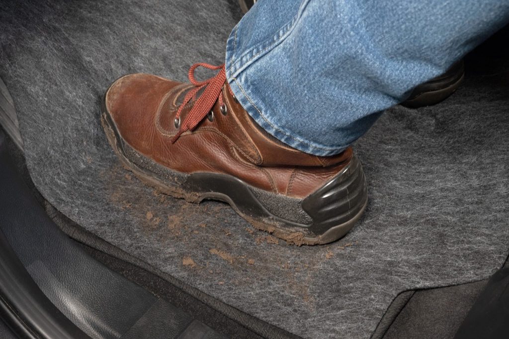 A person in dirty work boots on the car adhesive floor mat. Mud from the boots across the mat.