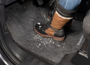 The car adhesive floor mat with a person and their snowy boots on the mat showing how it contains the mess.